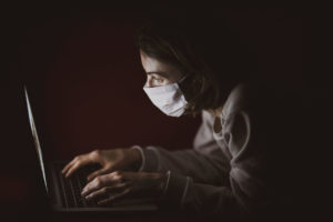 Worker with coronavirus PPE mask working on laptop